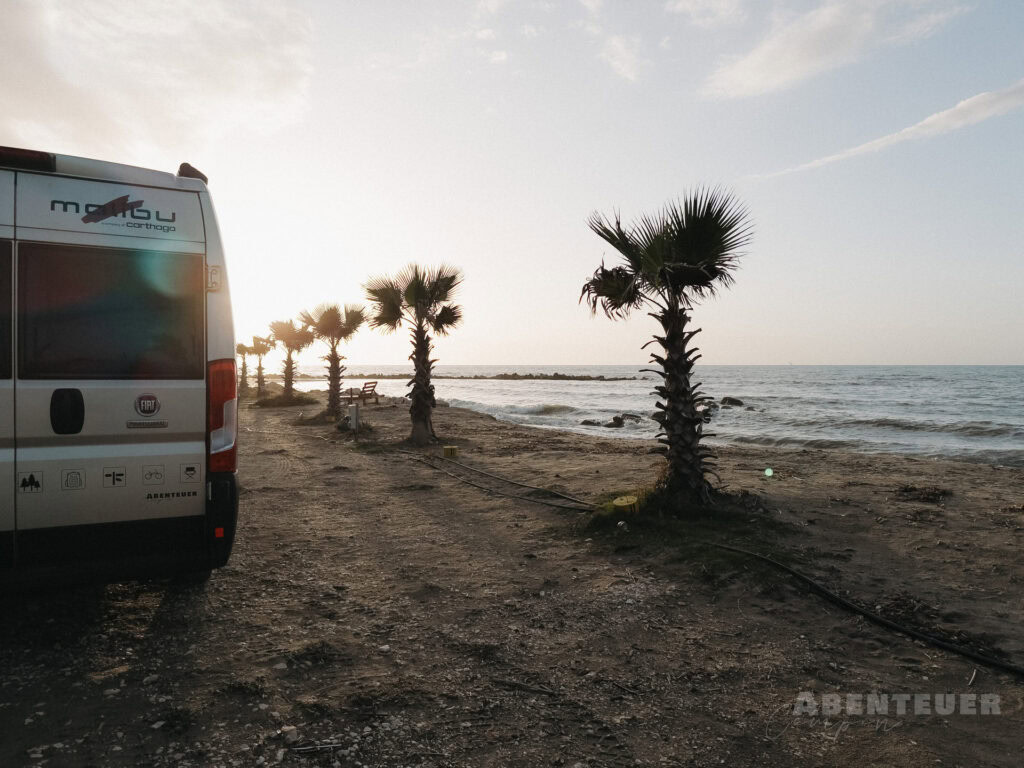 Abenteuercampen am Strand mit Palmen und Meerblick bei Sonnenuntergang.