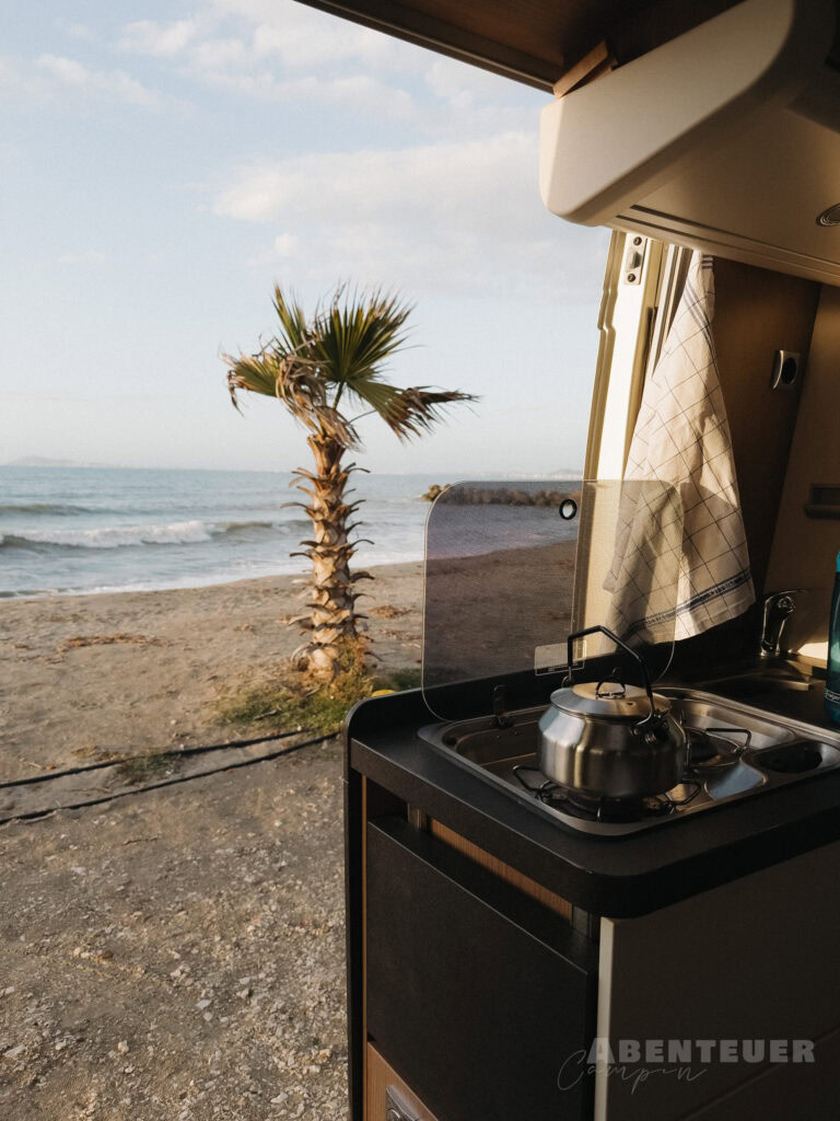 Blick aus dem Camper auf Strand und Palmen bei heißen Quellen.