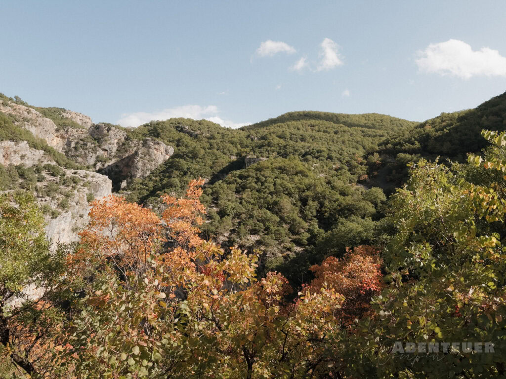Abenteuercampen inmitten der Natur bei heißen Quellen, umgeben von Bergen und bunten Herbstbäumen.