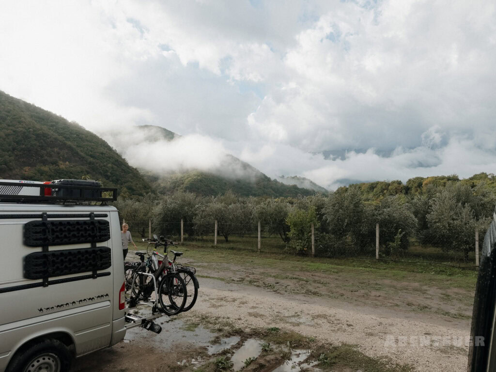 Camping bei heißen Quellen inmitten der Natur, umgeben von Bergen und Wolken.