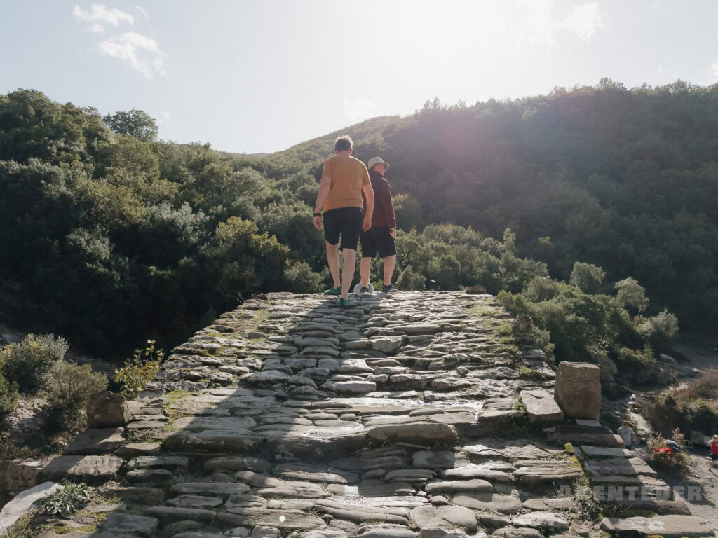 Zwei Personen beim Wandern auf einer alten Steinbrücke in der Natur.