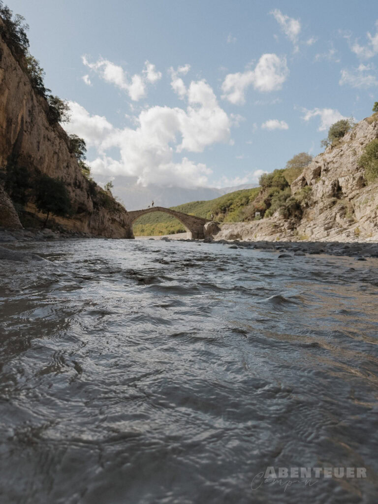 Fluss mit Brücke und umgebender Natur bei Tag, heiße Quellen in der Nähe.
