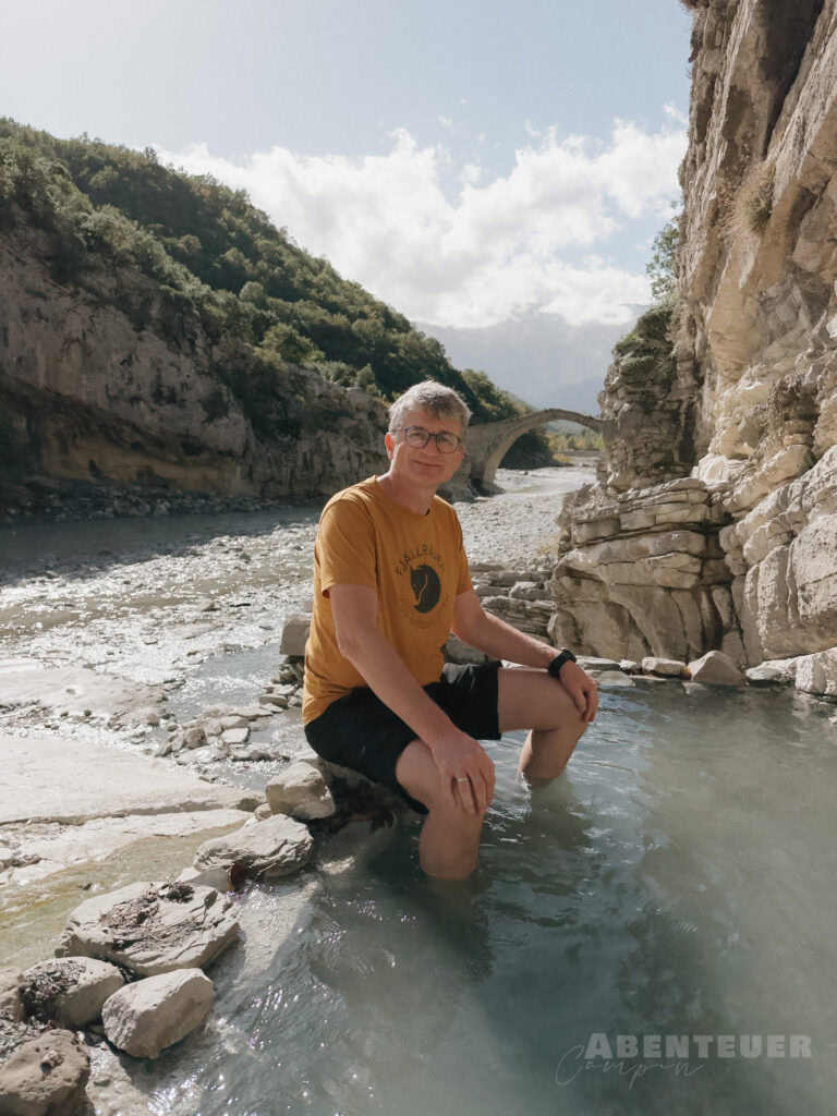 Mann in Thermalwasser bei Tag 15, umgeben von Bergen und Natur.